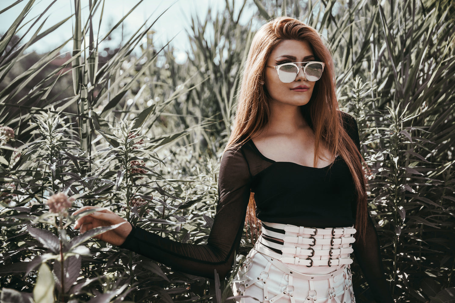 Lady in shades standing in bushy field.